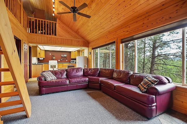 living room featuring ceiling fan, high vaulted ceiling, wooden ceiling, wooden walls, and light carpet