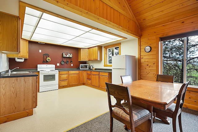 kitchen featuring white appliances, wooden walls, dark countertops, vaulted ceiling, and a sink