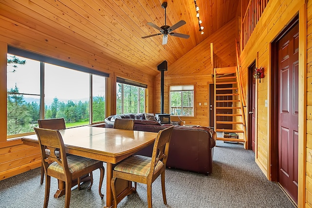 dining area with dark carpet, a wood stove, vaulted ceiling, wooden walls, and wooden ceiling