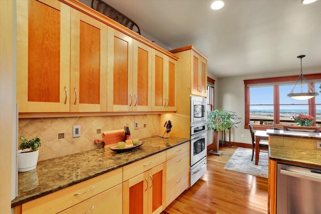 kitchen featuring appliances with stainless steel finishes, decorative backsplash, a warming drawer, dark stone countertops, and decorative light fixtures