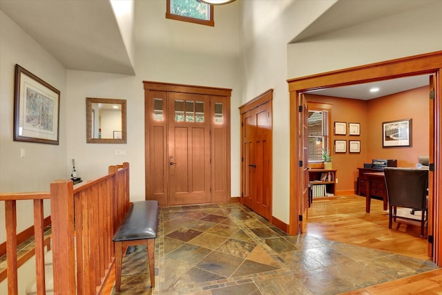 foyer entrance featuring stone tile flooring, a towering ceiling, and baseboards