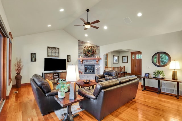 living room with arched walkways, ceiling fan, a stone fireplace, and light wood-style floors