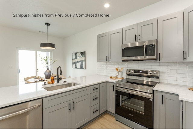 kitchen with backsplash, gray cabinets, stainless steel appliances, light countertops, and a sink