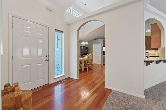 foyer entrance with baseboards, visible vents, arched walkways, dark wood-style flooring, and an inviting chandelier