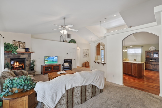 living area featuring lofted ceiling, visible vents, light carpet, and a stone fireplace