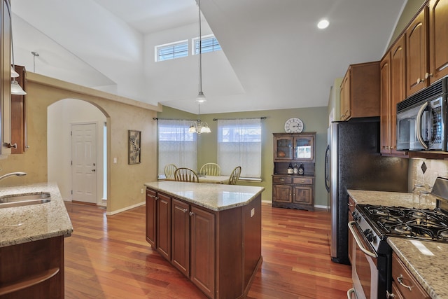 kitchen featuring light stone counters, a center island, arched walkways, a sink, and gas range