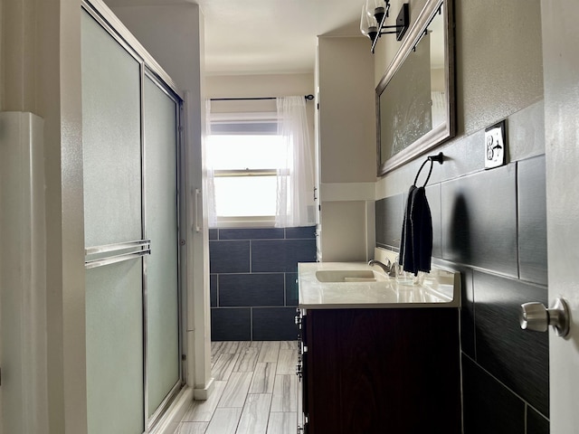 bathroom with wood tiled floor, a shower stall, vanity, and tile walls