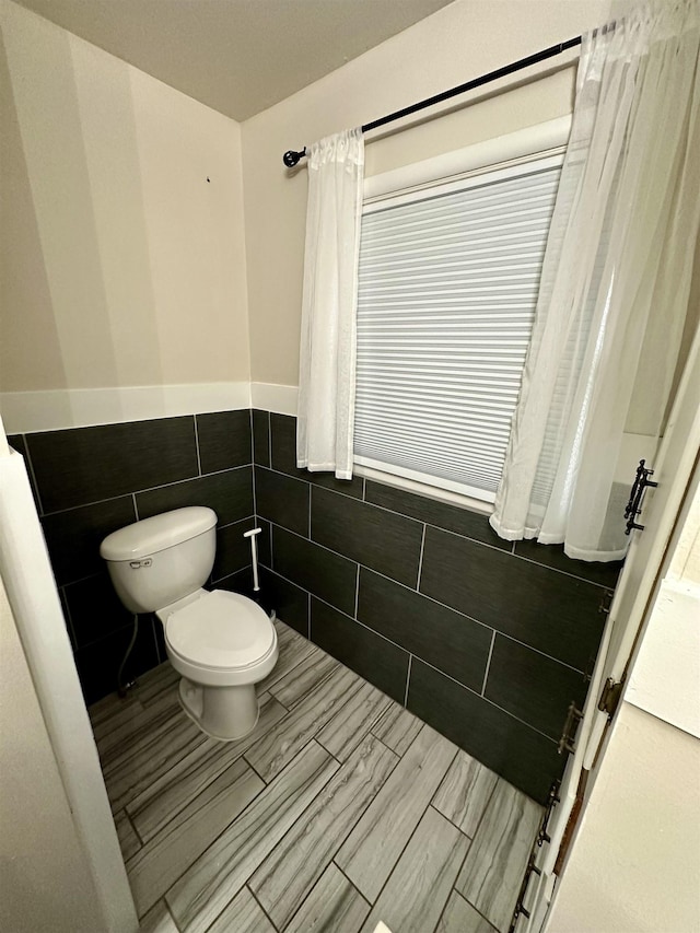 bathroom featuring toilet, tile walls, and wainscoting