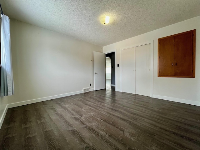 unfurnished bedroom featuring dark wood-style floors, a textured ceiling, visible vents, and baseboards