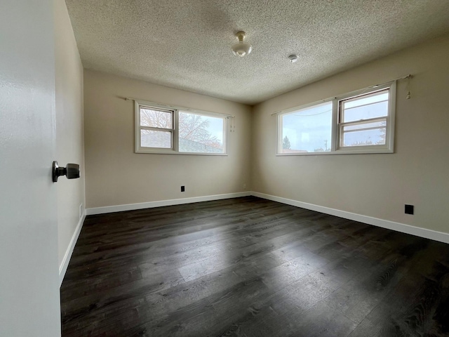 spare room featuring a wealth of natural light, dark wood finished floors, a textured ceiling, and baseboards