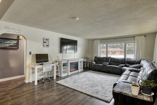 living area with a textured ceiling, arched walkways, dark wood finished floors, baseboards, and a glass covered fireplace