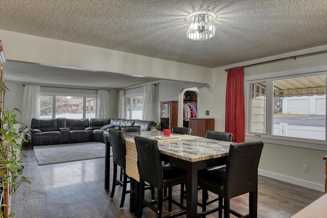 dining room with dark wood-style floors, arched walkways, a textured ceiling, and baseboards