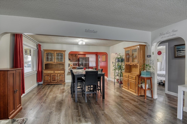 dining room with arched walkways, a textured ceiling, dark wood-style floors, and baseboards