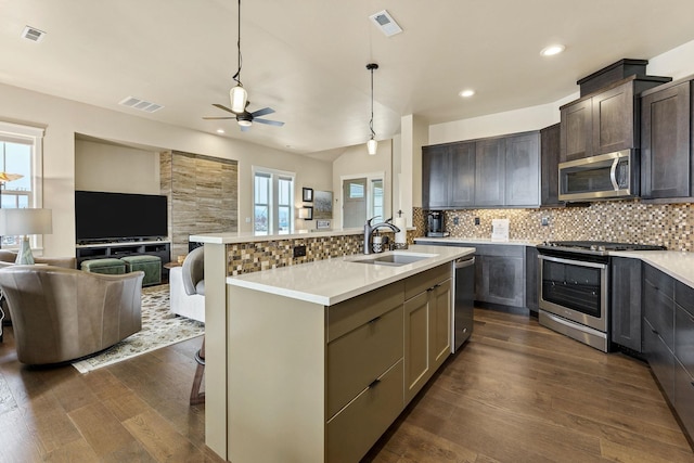 kitchen featuring a kitchen island with sink, stainless steel appliances, visible vents, open floor plan, and light countertops