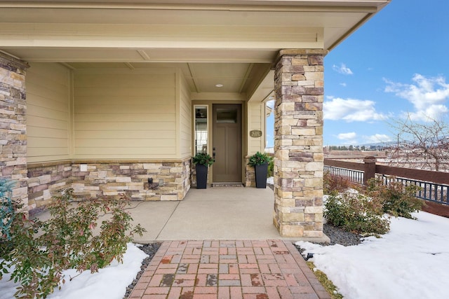 snow covered property entrance featuring stone siding