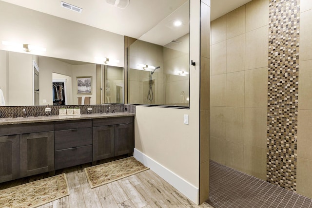 bathroom with double vanity, visible vents, wood finished floors, a walk in shower, and a sink