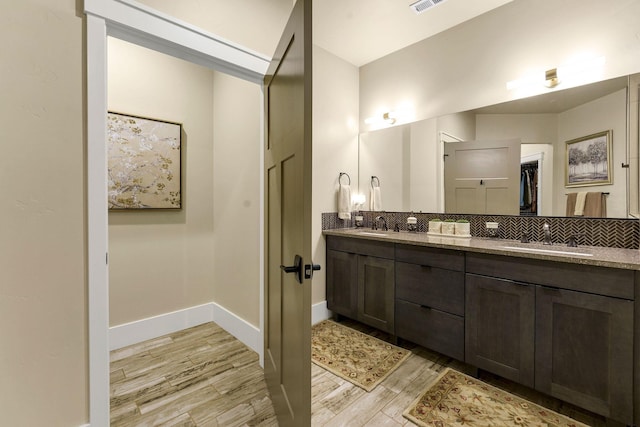 bathroom with double vanity, a walk in closet, a sink, and wood finished floors