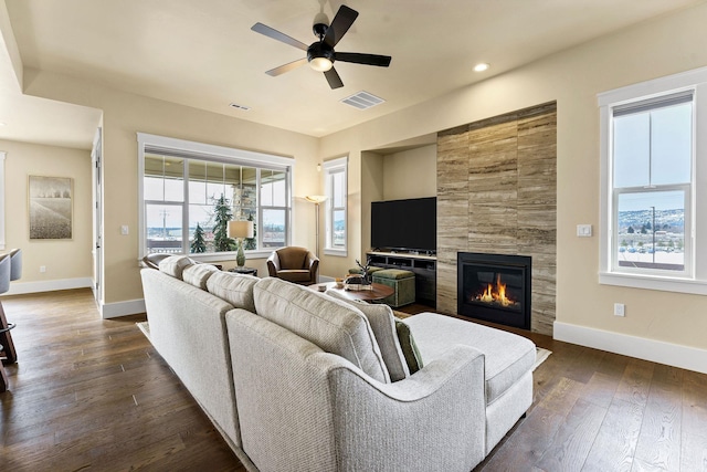 living room featuring ceiling fan, dark wood-style flooring, visible vents, baseboards, and a tiled fireplace