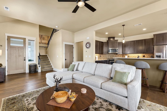 living area featuring dark wood-type flooring, a ceiling fan, visible vents, and stairs