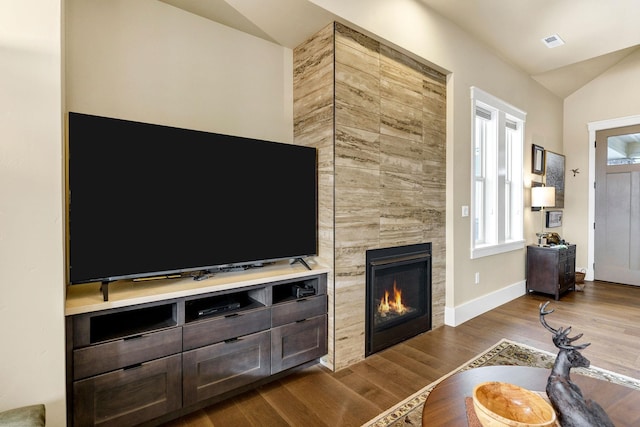 living room featuring visible vents, a tiled fireplace, vaulted ceiling, wood finished floors, and baseboards