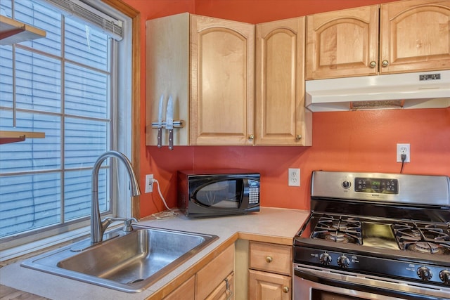 kitchen featuring under cabinet range hood, a sink, light countertops, stainless steel range with gas cooktop, and light brown cabinetry