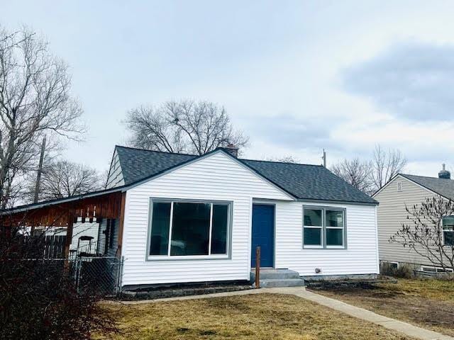 view of front facade featuring a front lawn, a shingled roof, and fence