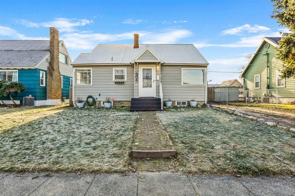 bungalow featuring entry steps, metal roof, cooling unit, fence, and a front lawn