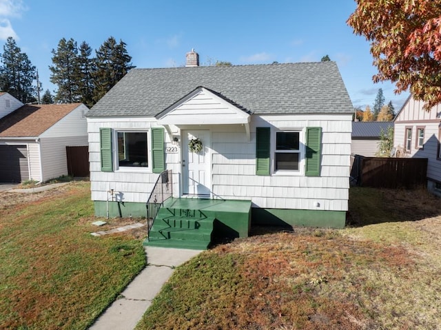 bungalow-style home featuring a shingled roof, a chimney, and a front lawn