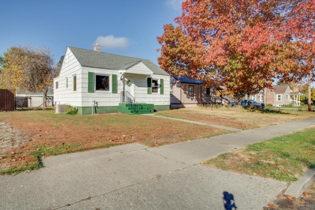 bungalow-style home with central air condition unit, a shingled roof, a chimney, and a front lawn