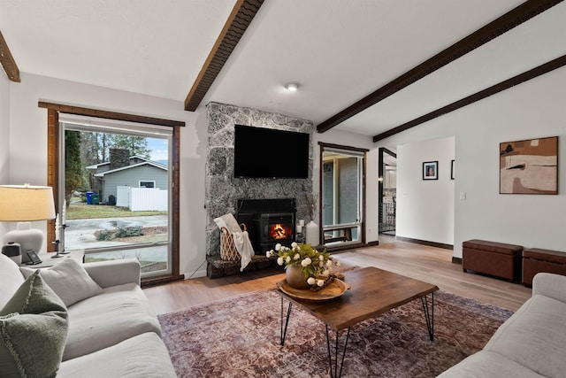 living area featuring a stone fireplace, baseboards, lofted ceiling with beams, and light wood finished floors