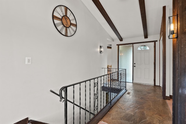 interior space with beamed ceiling, an upstairs landing, and stone tile flooring