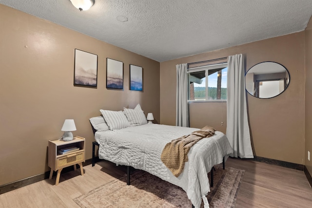 bedroom with a textured ceiling, wood finished floors, and baseboards