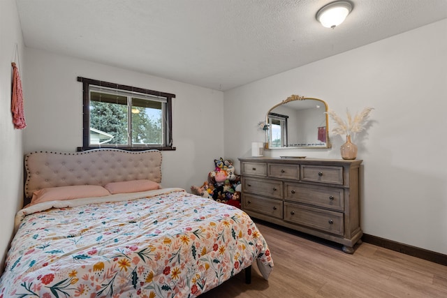 bedroom featuring a textured ceiling, baseboards, and light wood-style floors