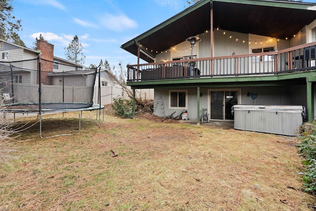 back of property with a trampoline, fence, a hot tub, and a deck