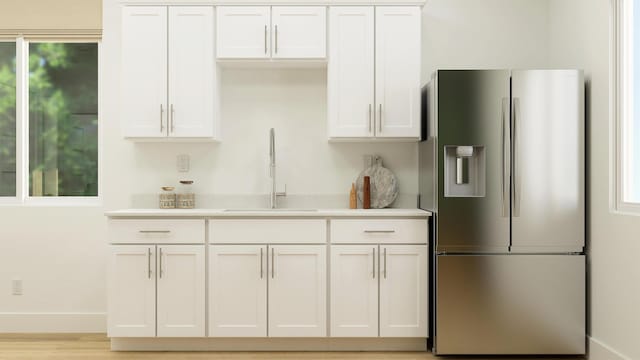 kitchen featuring a sink, baseboards, white cabinets, light countertops, and stainless steel fridge