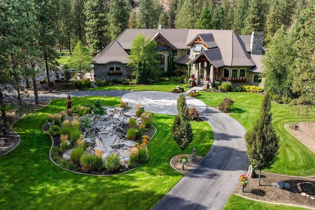 exterior space with aphalt driveway, stone siding, a tile roof, and a chimney