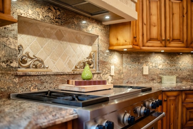 kitchen featuring tasteful backsplash, stainless steel range with gas cooktop, light stone countertops, and brown cabinets