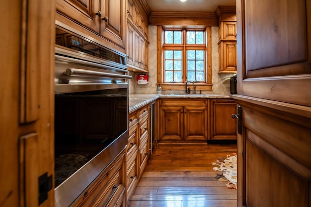 kitchen with dark wood-style floors, a sink, stainless steel oven, and brown cabinets