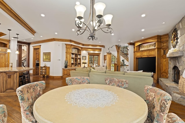 dining area featuring ornamental molding, dark wood-style flooring, an inviting chandelier, a fireplace, and recessed lighting