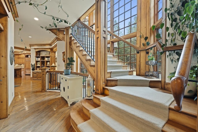 stairway with a high ceiling, ornamental molding, wood finished floors, and recessed lighting