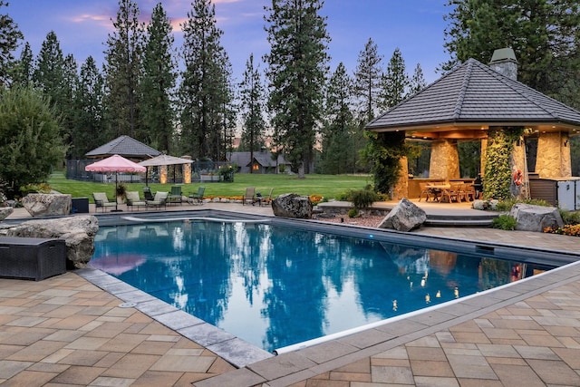 pool at dusk featuring a gazebo, a lawn, a patio, and an outdoor pool