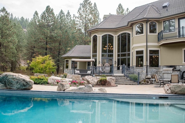 back of house with stucco siding, a patio area, stone siding, an outdoor pool, and a tiled roof