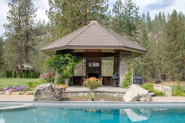 view of pool featuring an outdoor stone fireplace and a gazebo