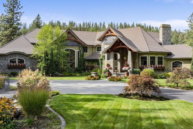 view of front facade with aphalt driveway, stone siding, a chimney, and a front lawn