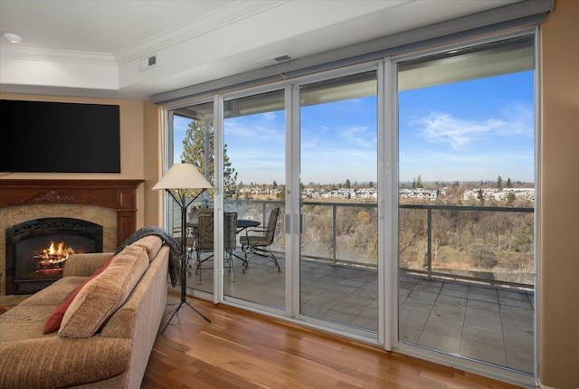 doorway with a lit fireplace, wood finished floors, visible vents, and crown molding