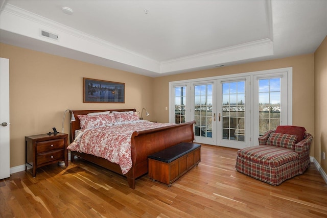 bedroom with light wood-type flooring, access to exterior, multiple windows, and a raised ceiling