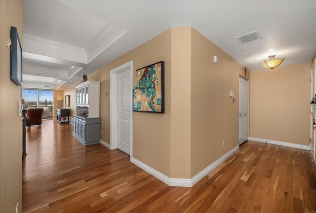 corridor with baseboards, visible vents, wood finished floors, and ornamental molding