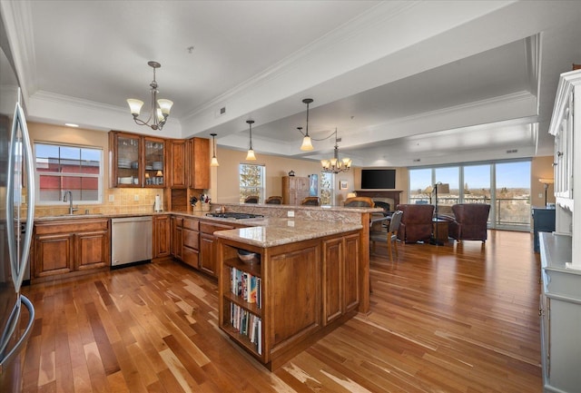 kitchen featuring brown cabinetry, a raised ceiling, a peninsula, stainless steel appliances, and a notable chandelier