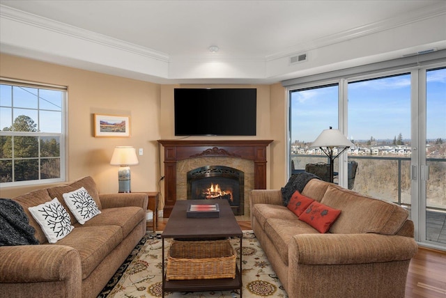 living room with a wealth of natural light, visible vents, crown molding, and wood finished floors