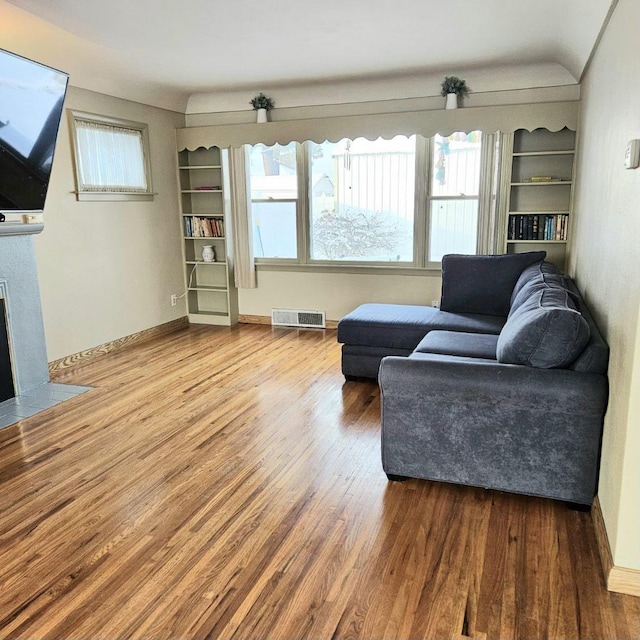 living area with built in features, visible vents, a fireplace with flush hearth, wood finished floors, and baseboards